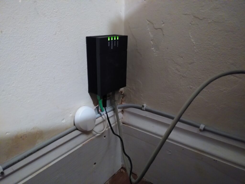 Black box above skirting board with status lights at the top, and cables at the bottom.