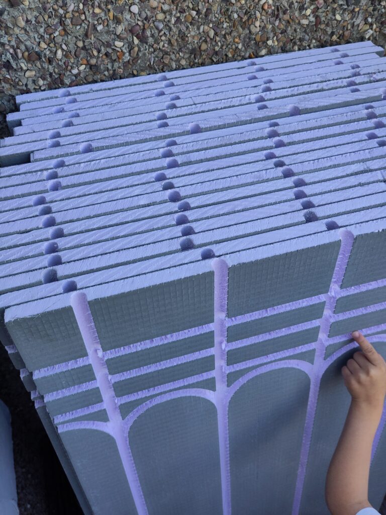 Insulated boards standing vertically against outside wall. Grooves for adding the pipes in.