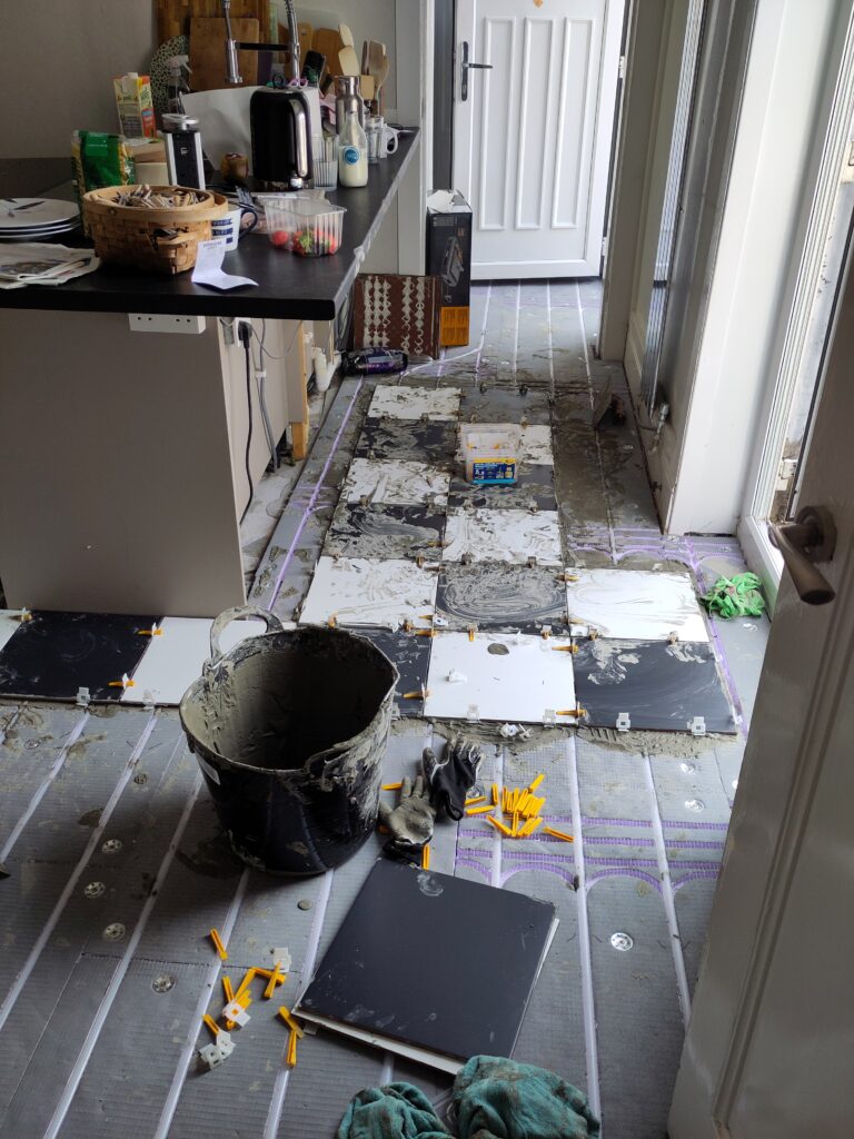 20 black and white tiles laid on the floor. Island kitchen counter on the left. Pail used for adhesive in foreground.