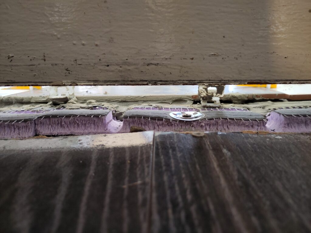 Gap under the door, laminate floor in another room, can see backer board, and tiles, with a small gap under the door.