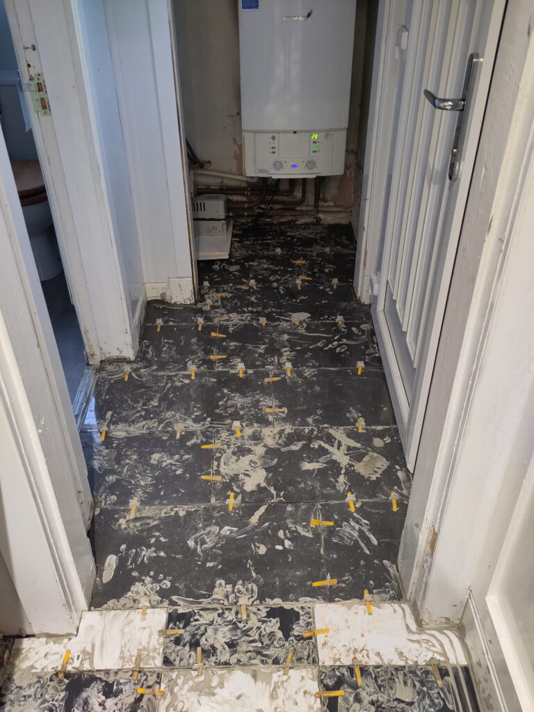 In foreground black and white tile. Behind grey granite tiles. Background gas boiler. Right hand side is a door.